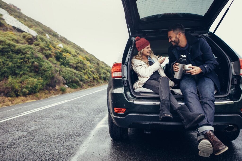 Couple sitting in the back of an SUV with the trunk open. Stopping on a road trip.