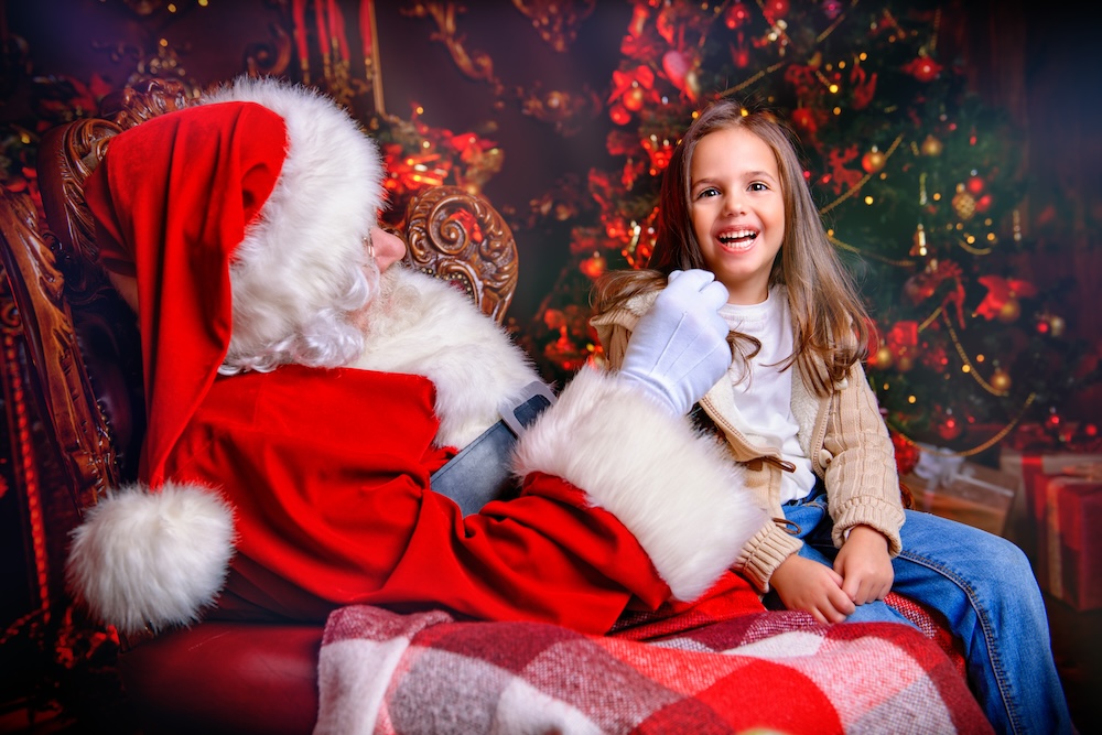 A young girl smiling while sitting in Santa Claus's lap