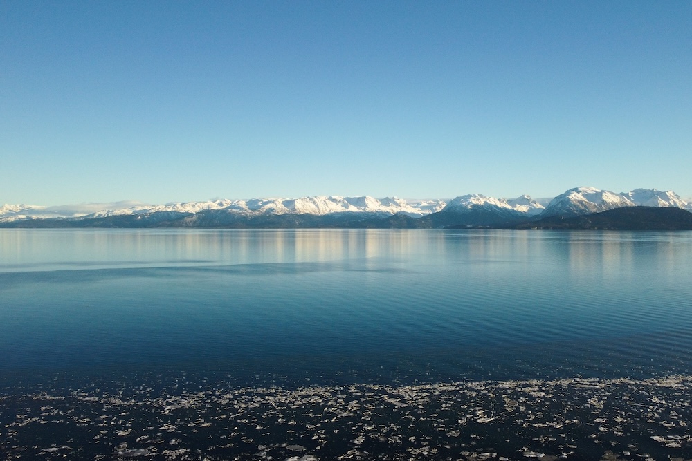 A calm bay with a clear sky and snowy mountains in the background