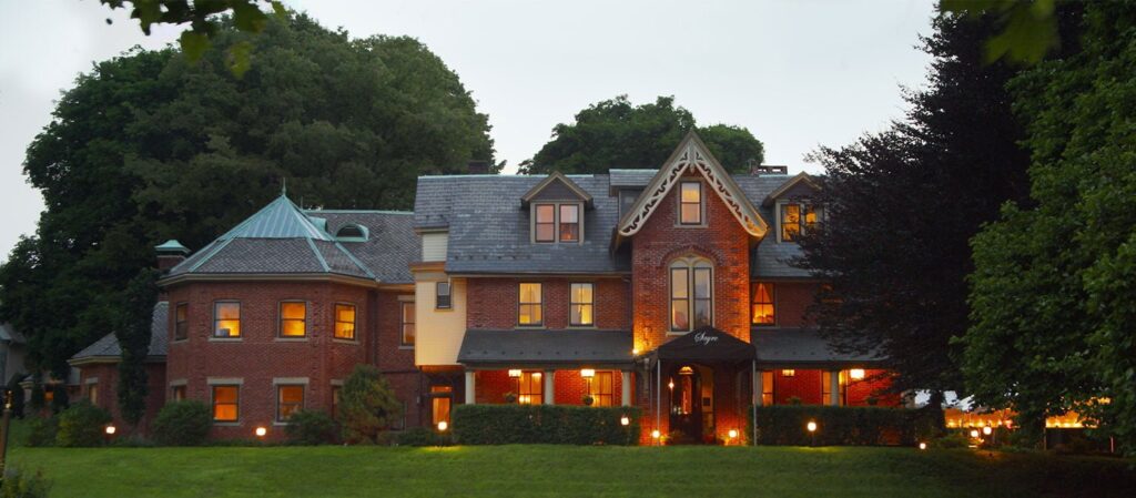 The lights of Sayne Mansion illuminate its red brick exterior during dusk at summer in Bethlehem.