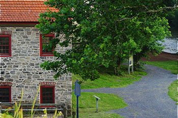 a gray stone building with red window panes next a road and green grass.