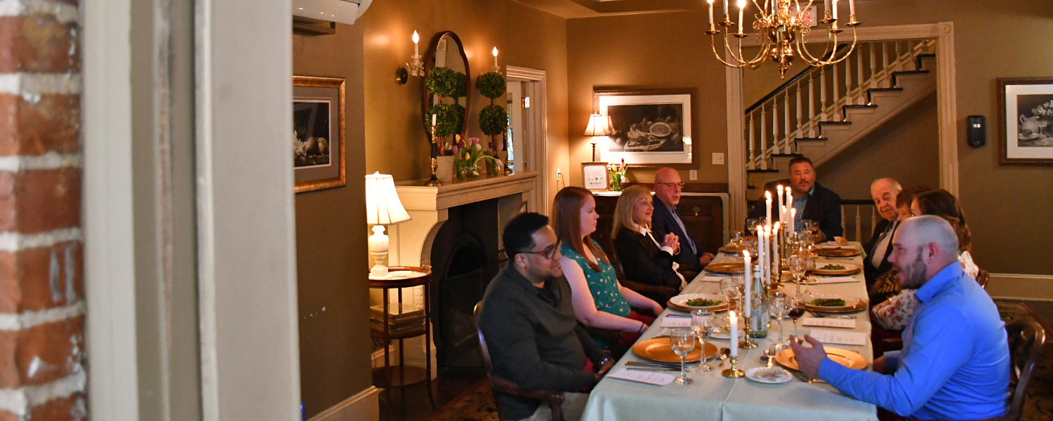 a group of nine sits at the Founder's Table, a private dining room with soft lighting and candles on a long table.