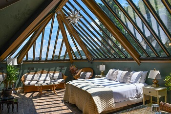 a suite with green walls and a king size bed with a red couch and love seat to its right, beneath a skylight