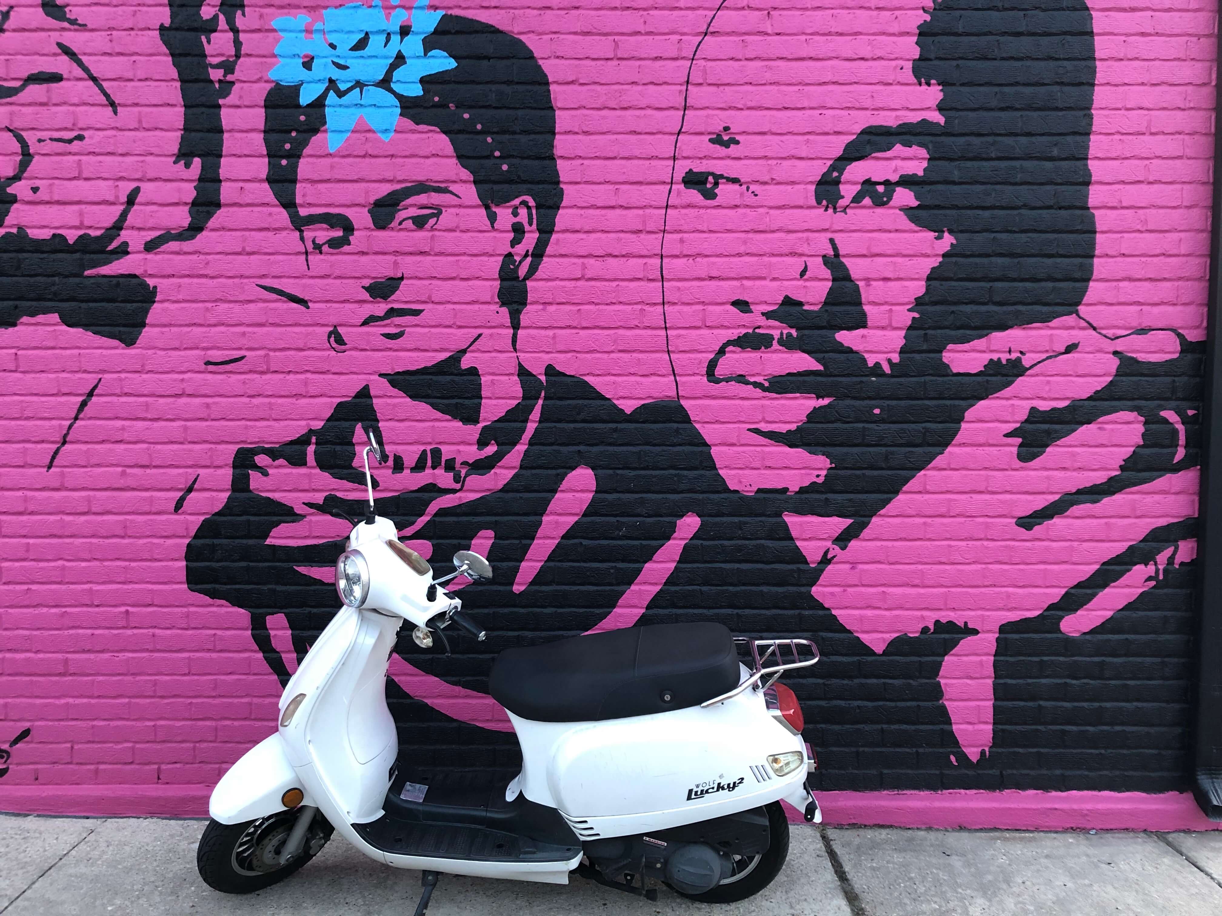A white motor scooter in front of a pink mural