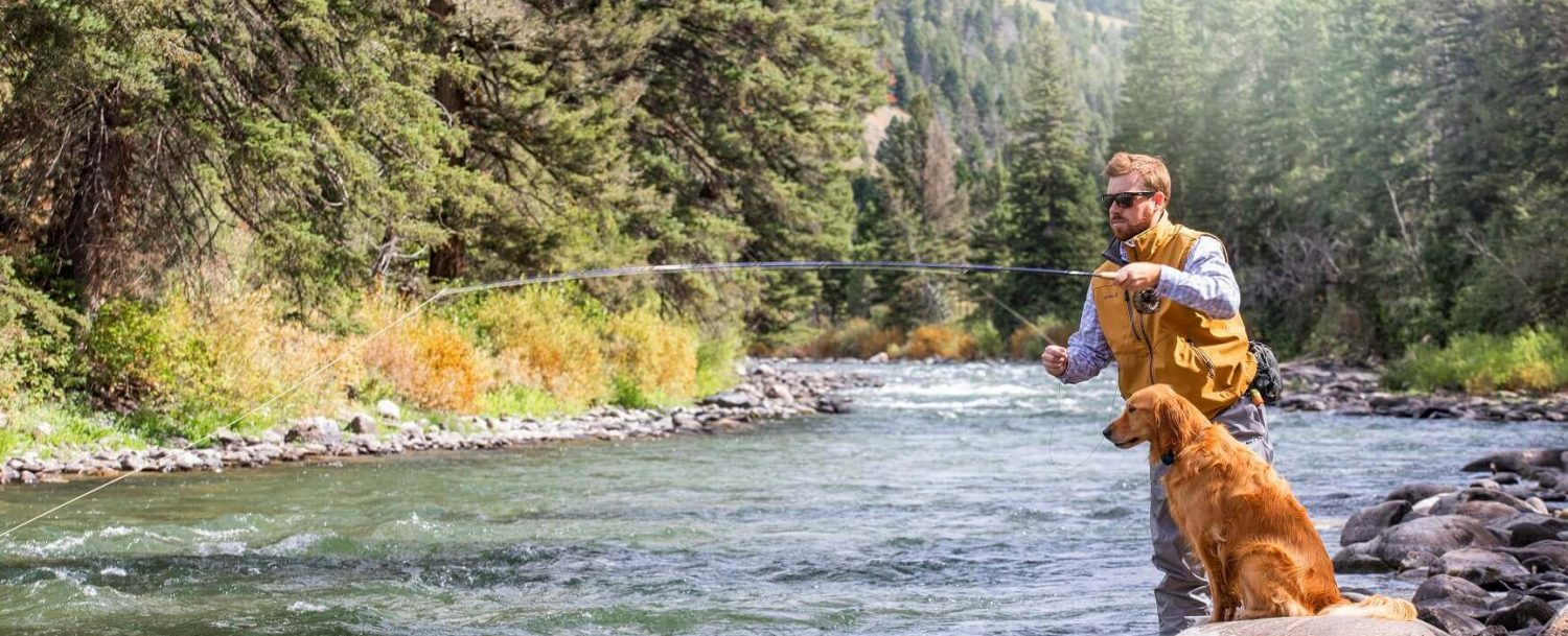 man fly fishing with dog sitting beside him