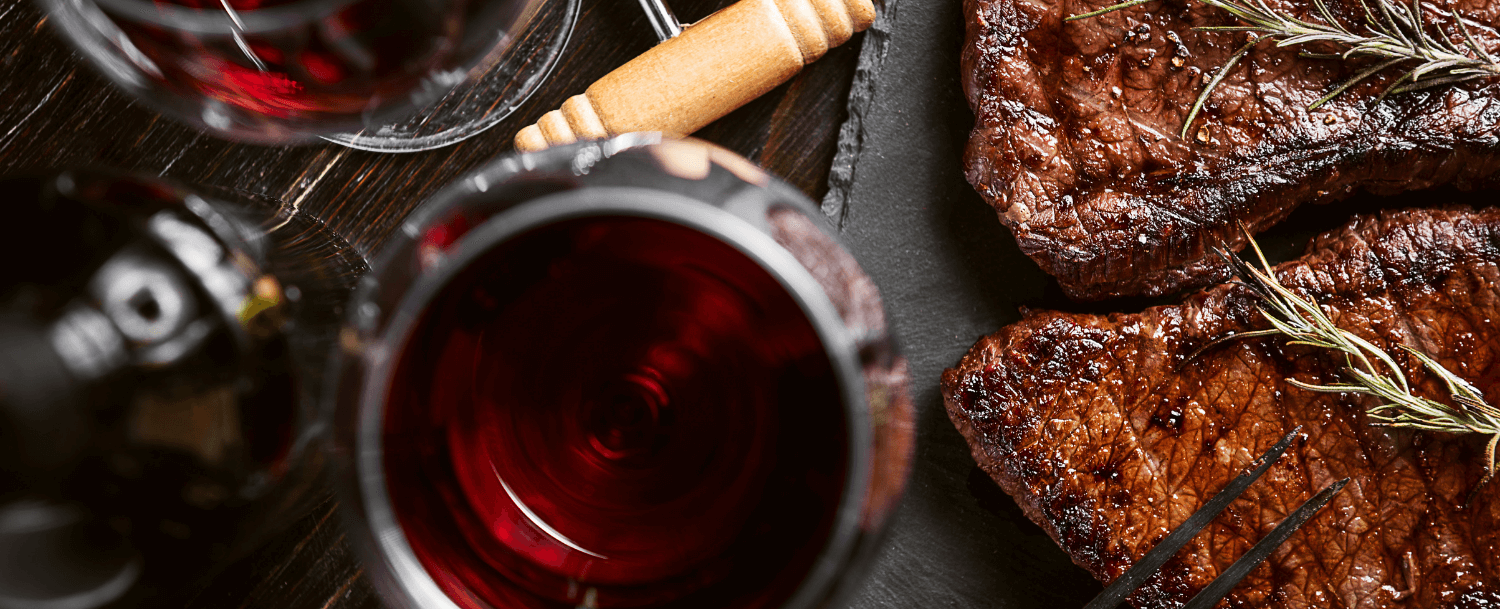 close up of steak and red wine in wine glasses