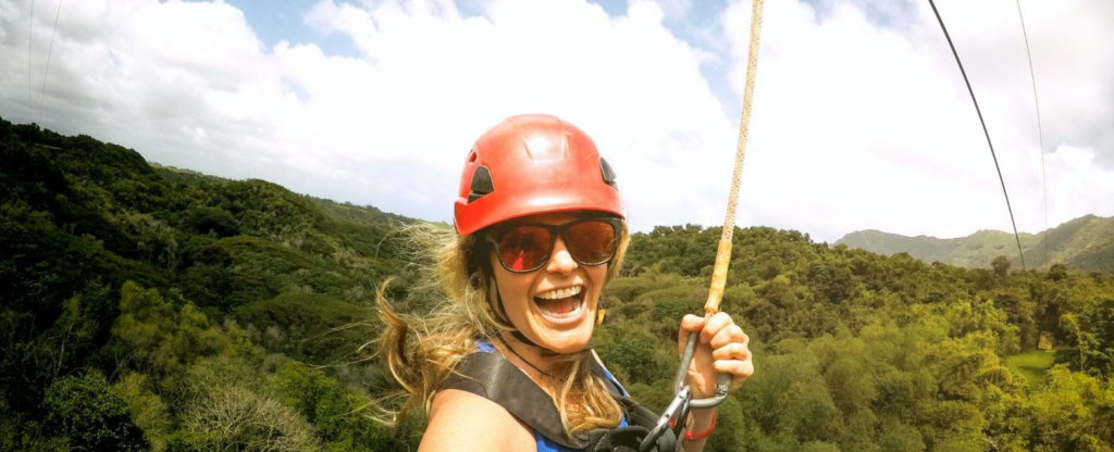 woman smiling on a zip line above the trees