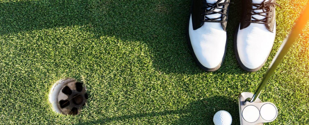 close up of golf shoes and putter on a golf green