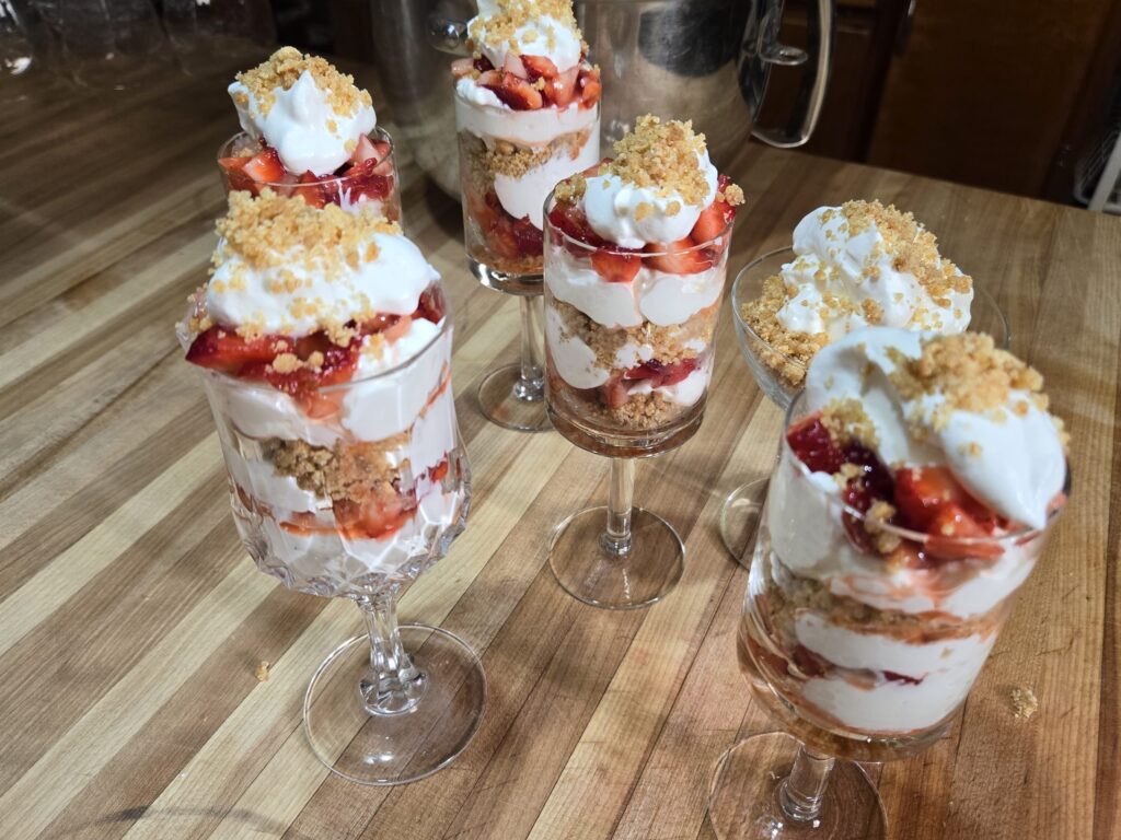 Six strawberry parfaits in glass dish on silver platter.