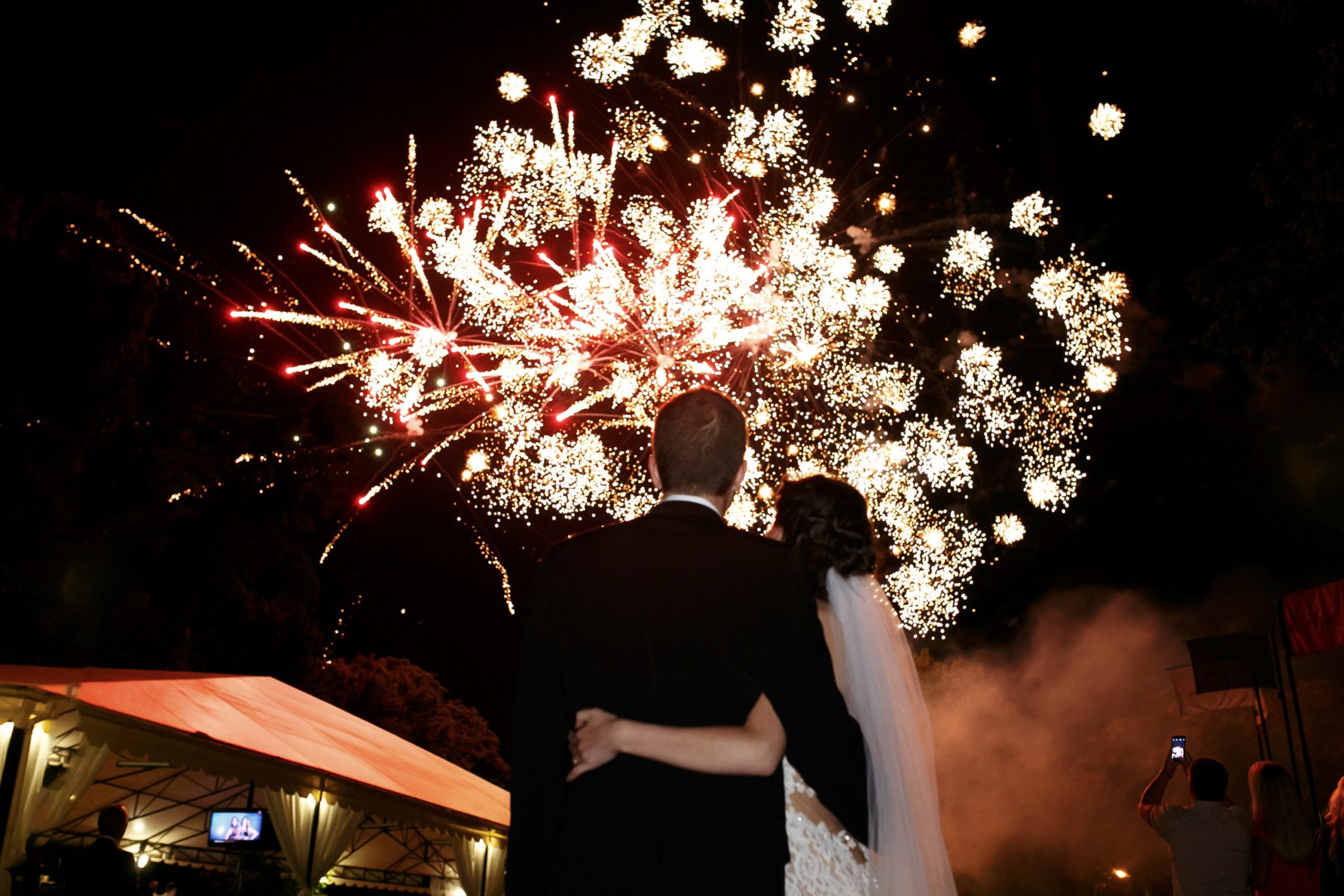 Happy hugging bride and groom watching beautiful colorful fireworks