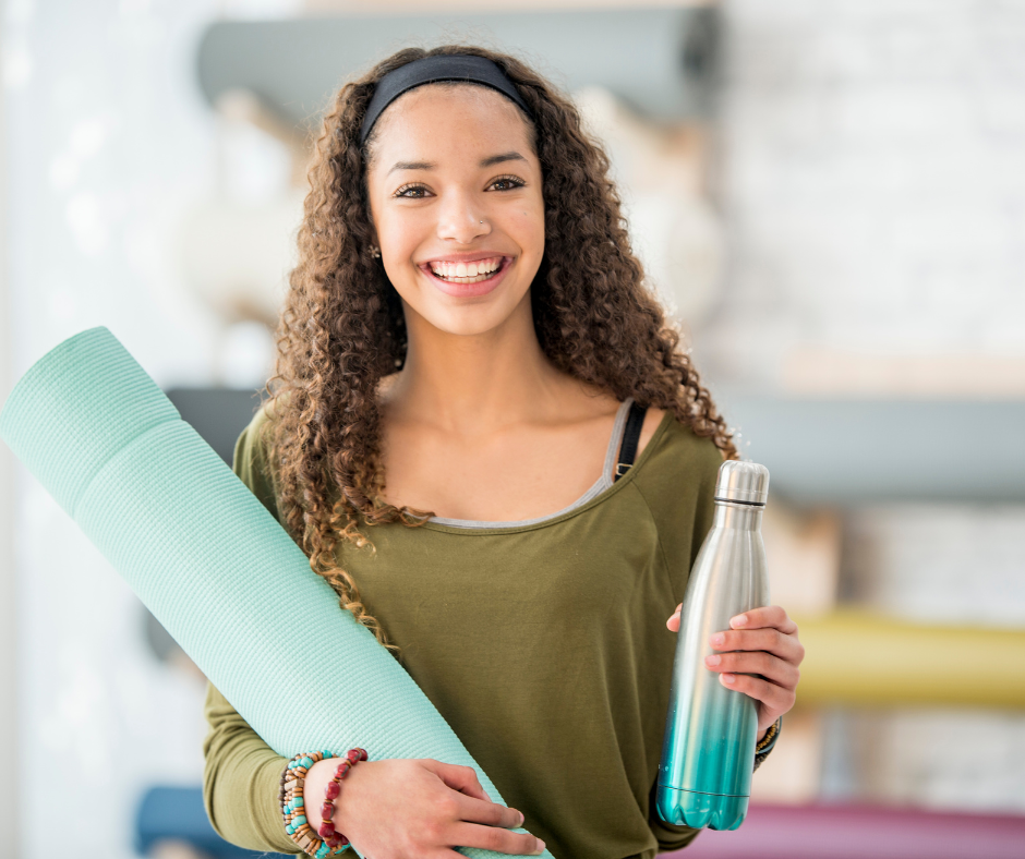 Woman carrying yoga mat and water bottle smiling