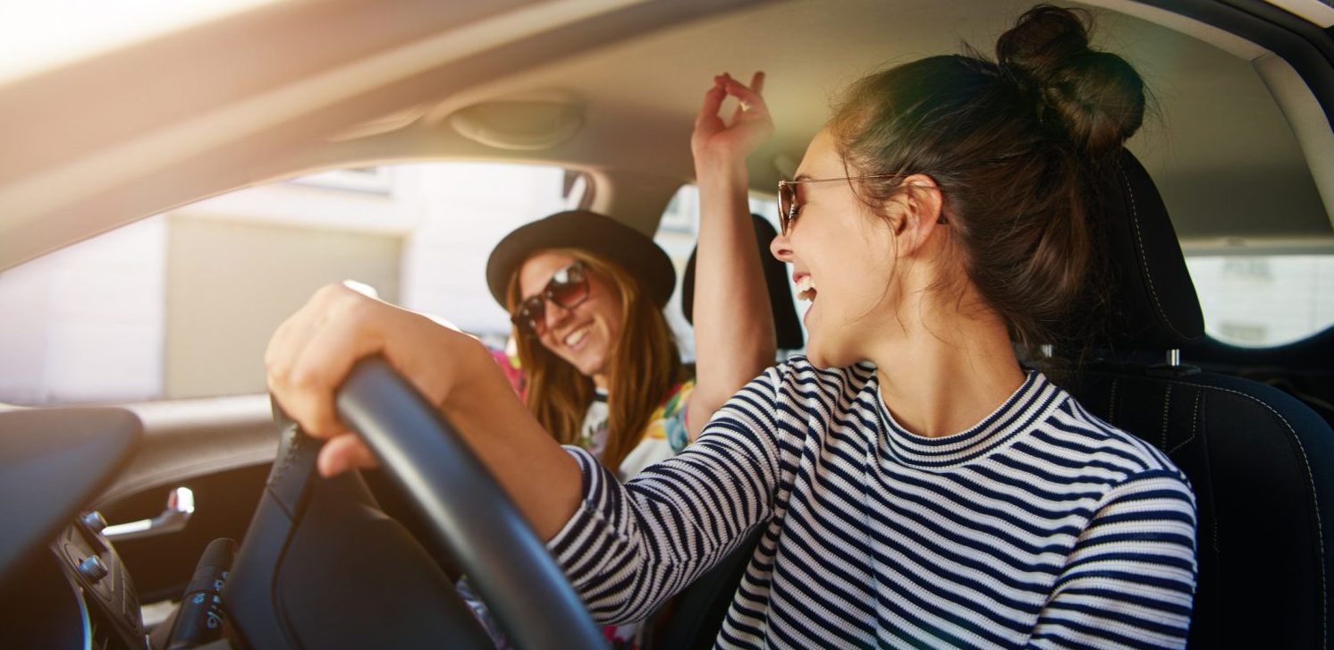 Two young women having fun driving along the street laughing and joking with the driver distracted looking at her passenger - Weekend Getaways in PA for Girlfriends