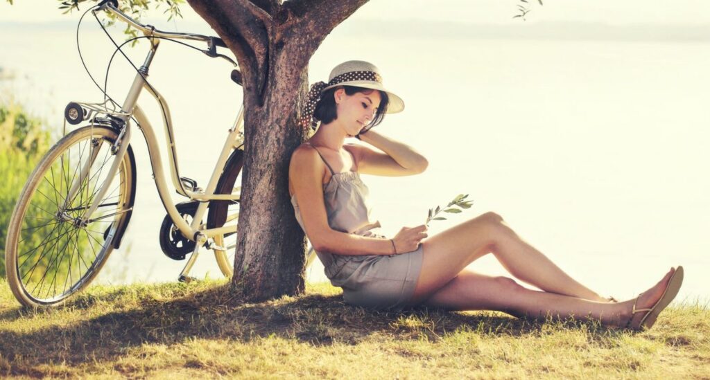 Beautiful dormant woman in love waiting under a tree by the lake with a bike by her side