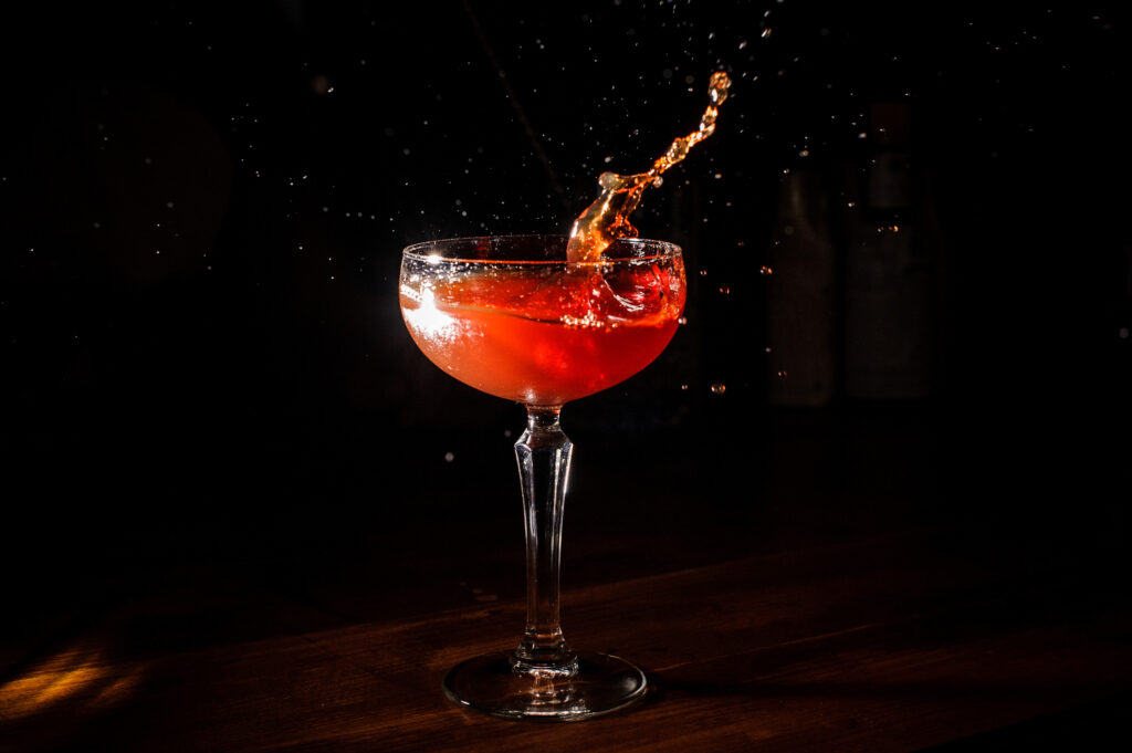 red orchard cocktail splashing into glass on black background