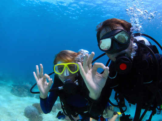 Couple scuba diving and giving the okay hand sign at Anthony's Key Resort in Roatan, Honduras.