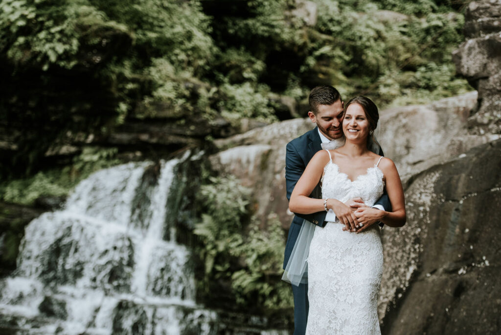 groom embraces bride at waterfall