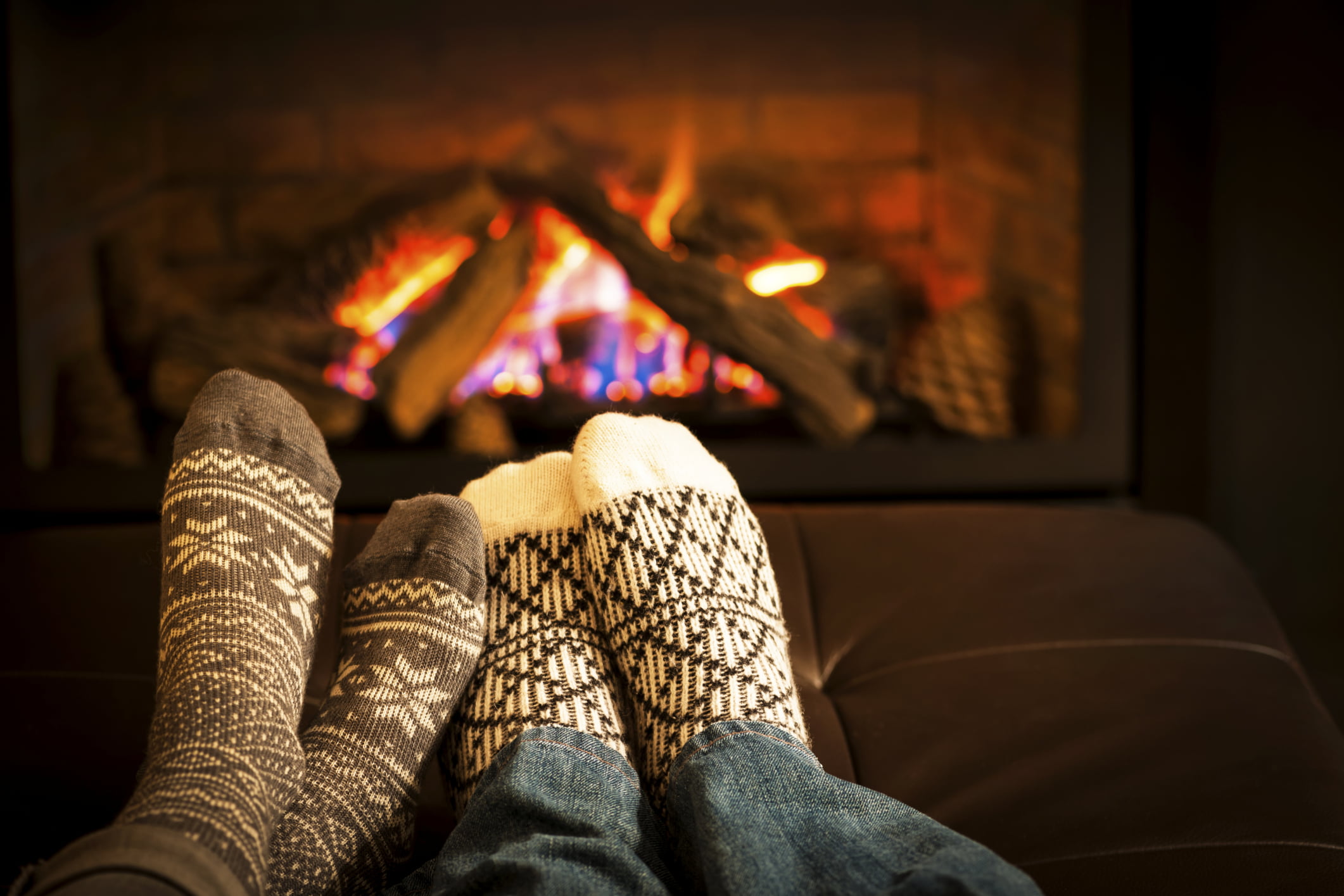 2 pair of feet in cozy socks warming up by a roaring fire