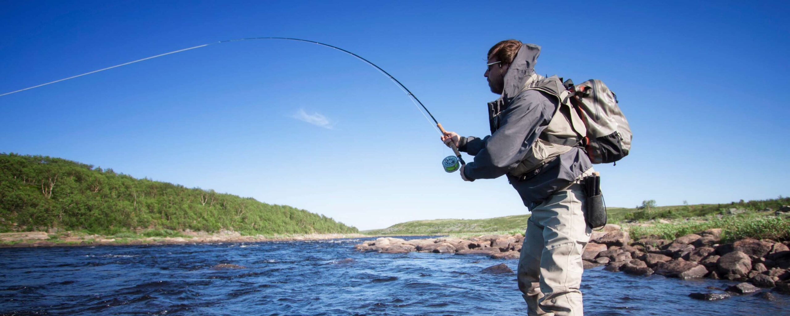A man standing in a river fly fishing on a cloud free day
