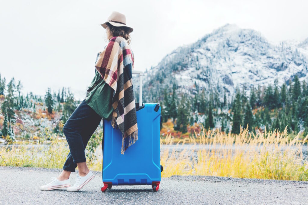 Traveling woman wearing poncho and hat sitting on her bright blue suitcase near stunning mountain wilderness. Wanderlust and boho style (Traveling woman wearing poncho and hat sitting on her bright blue suitcase near stunning mountain wilderness. Wand