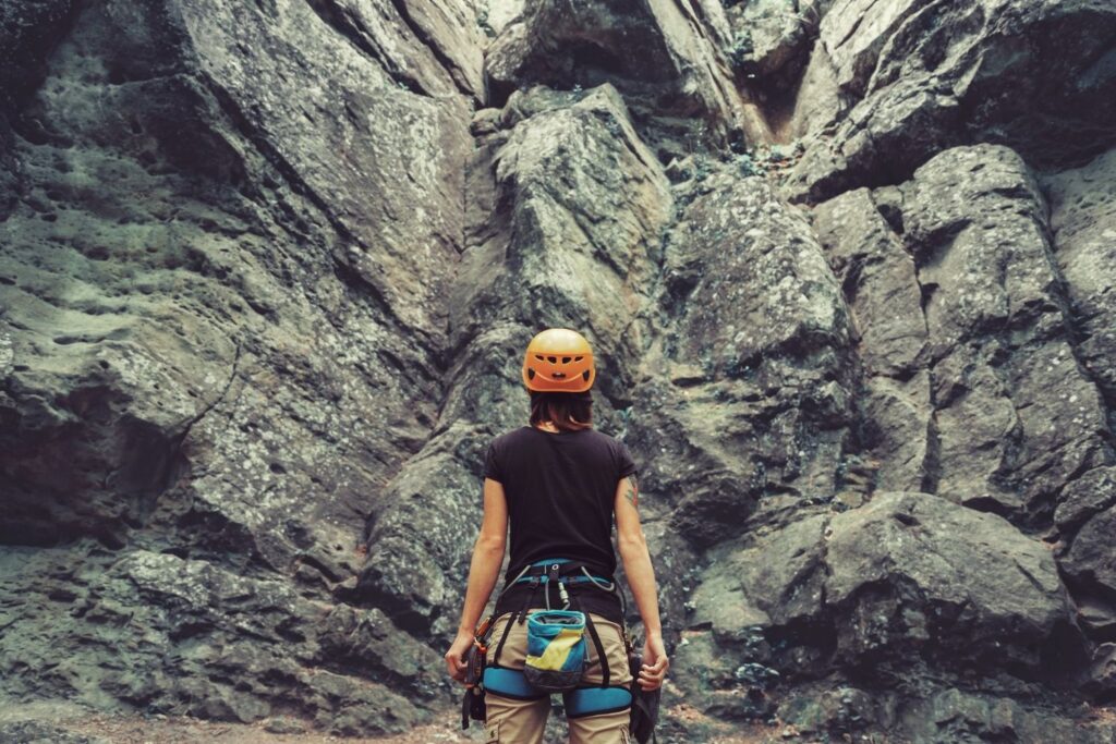 Woman in gear standing in front of a rock climbing wall.