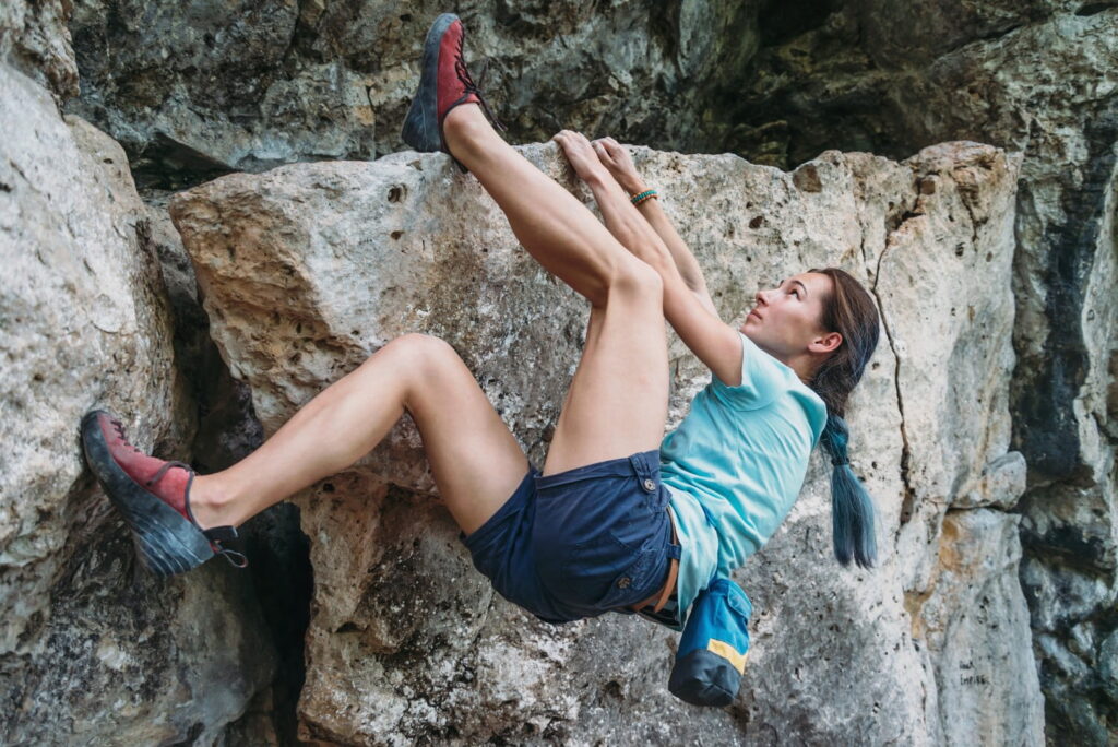 Beautiful sporty young woman started to climb the rock outdoor, bouldering