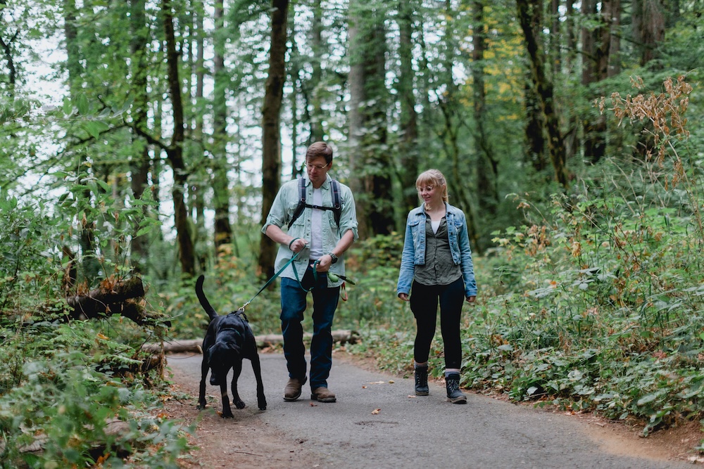 couple hiking through PNW forest with their black lab dog