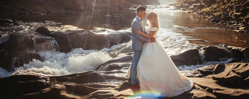 bride and groom standing on rocks with a rushing mountain river flowing behind them