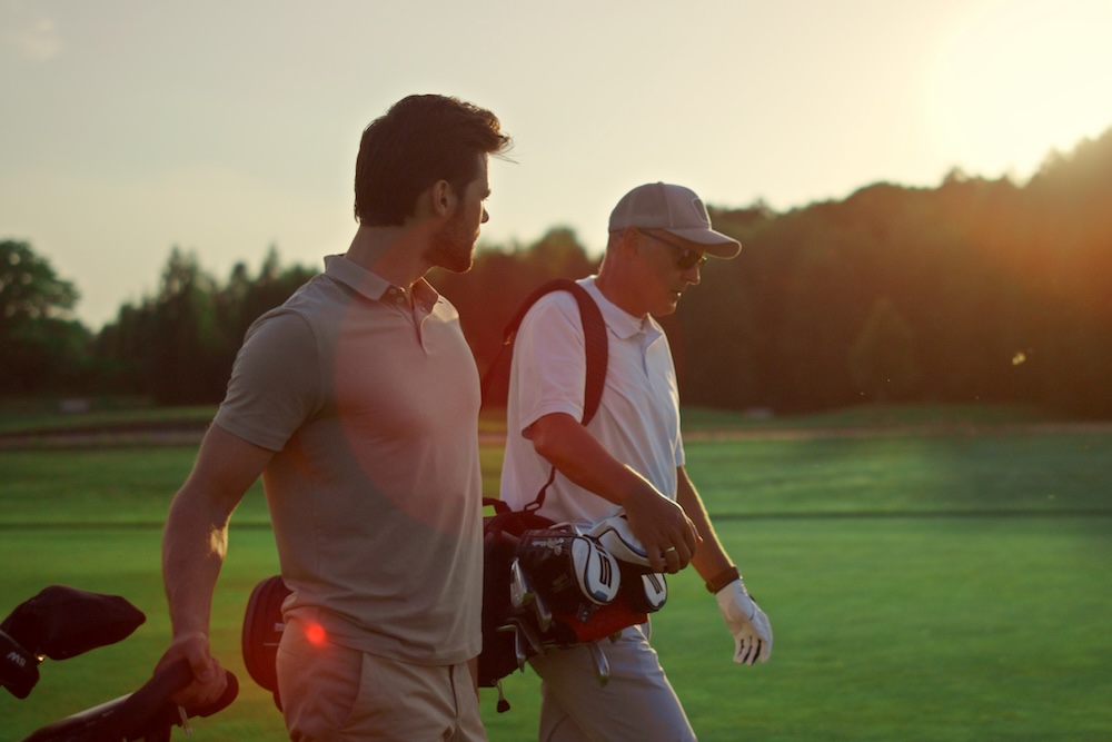 two men walking on a golf course at sunset.