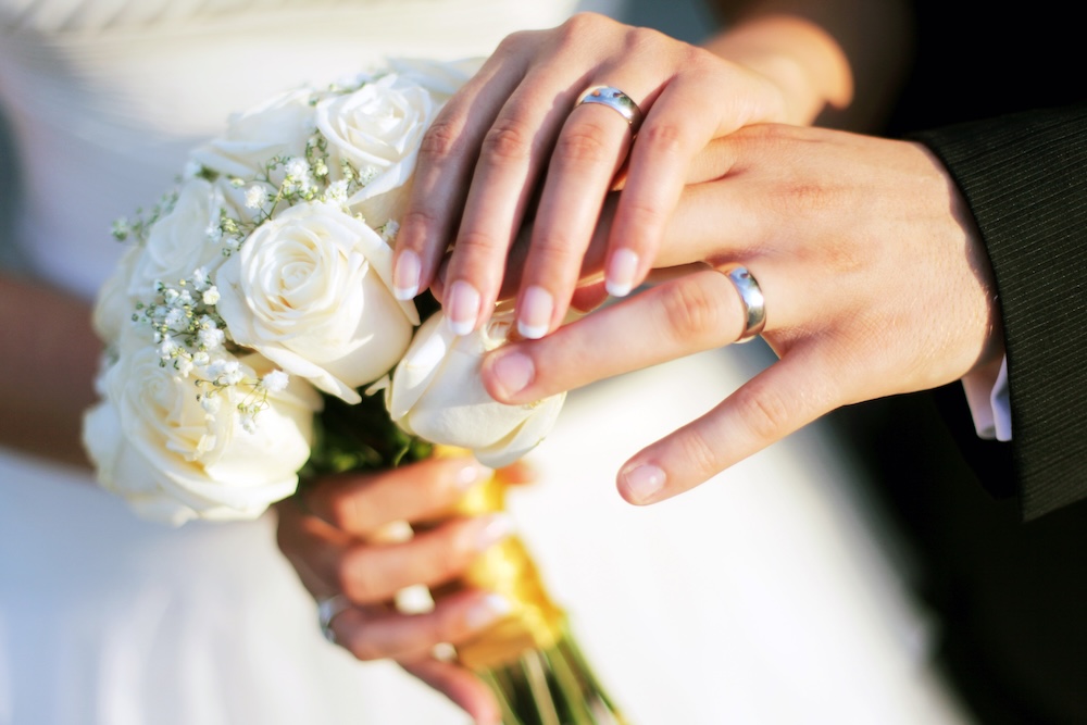 Wedding rings, bouqet and hands holding close up