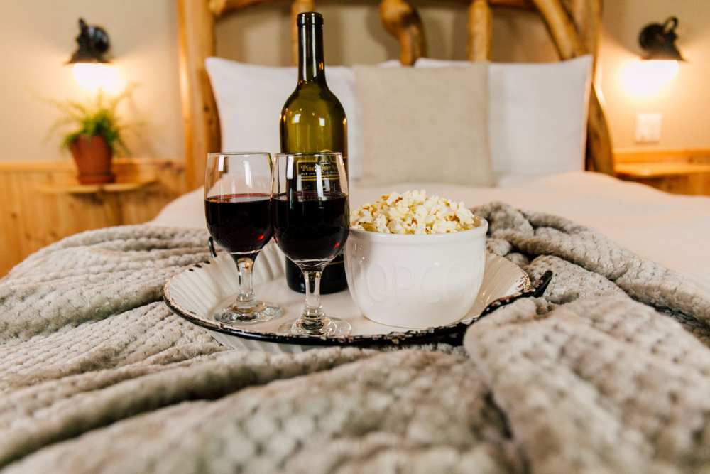 popcorn and wine on tray on comfortable bed
