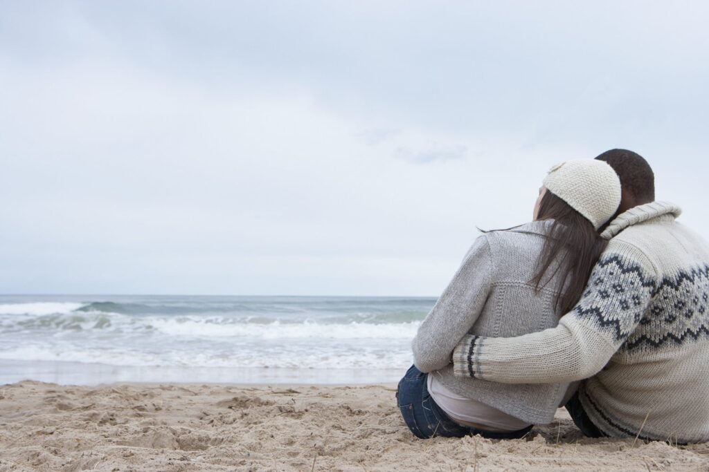 Loving couple sitting and hugging on winter beach from behind