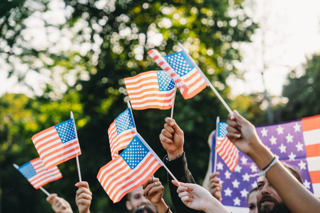 A group of people is waving small American flags at sunset. Concept for various topics like Happy Veterans Day, Labour Day, Independence Day.